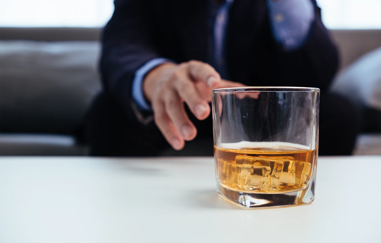 Man sträcker sig efter glas med alkohol – symbol för kampen att sluta dricka alkohol.